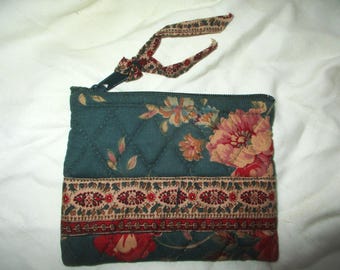May include: A quilted green fabric coin purse with a floral print and a brown and beige trim. The purse has a zipper closure and a black fabric strap.