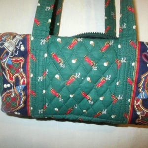 May include: A quilted green handbag featuring a repeating pattern of red golf bags and white golf balls. The side panels are dark blue with a detailed print of golf clubs, golf bags, and plaid accents. The bag includes two fabric handles.