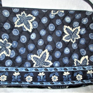 May include: A navy blue quilted crossbody bag with a repeating pattern of white maple leaves and blue circles. The bottom border features a floral design with white flowers and blue accents. The bag has a zipper closure and a matching strap.