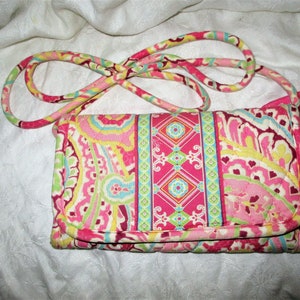 May include: A pink, yellow, and green quilted crossbody purse with a paisley pattern. The purse has a long strap and a zipper closure.