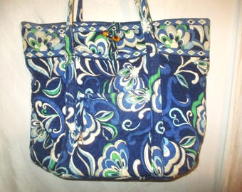 May include: A blue and white floral tote bag with a brown handle. The bag has a quilted design and is made of fabric.