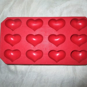 May include: A red silicone mold with twelve heart-shaped cavities. The mold is rectangular with rounded corners. The hearts are evenly spaced and have a smooth, glossy finish. Ideal for making chocolates or candies.