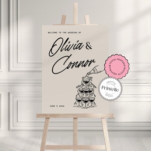 May include: A wedding welcome sign with a champagne bottle pouring into a tower of champagne glasses. The sign reads "Welcome to the wedding of Olivia & Connor" and "June 5, 2026".