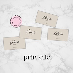 May include: Four beige place cards with black calligraphy that reads "Olivia Connor" and "Table No." followed by a number. The cards are arranged on a white marble surface. A pink and black circular stamp with the text "Swap Out Three Styles Printelle" is in the upper left corner of the image.