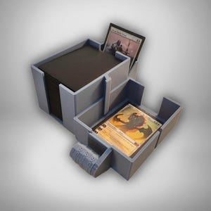 Könnte beinhalten: Hellblaue Kartenaufbewahrungsbox mit mehreren Fächern. Die Box enthält einen Stapel schwarzer Karten und mehrere einzelne Karten. Ein Zahlenschloss ist auf der Vorderseite sichtbar. Für Sammelkartenspiele konzipiert.