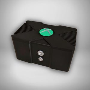 Könnte beinhalten: Eine schwarze, rechteckige Konsole mit einem grünen und silbernen Logo auf der Oberseite. Die Konsole hat zwei silberne Knöpfe auf der Vorderseite. Die Oberseite der Konsole hat ein strukturiertes Design.
