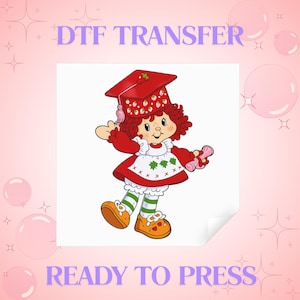 May include: A DTF transfer ready to press featuring a cartoon character with red hair wearing a red graduation cap with strawberry patterns, a red dress with a white apron, green and white striped stockings, and orange shoes, holding a diploma.