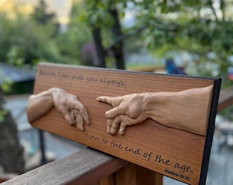 May include: A wooden plaque featuring a carved relief of two hands nearly touching, with the text "Behold, I am with you always, even to the end of the age. Matthew 28:20." The plaque is stained a reddish-brown color and has a black border.