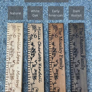 May include: Four wooden growth charts with different stain options labeled Natural, White Oak, Early American, and Dark Walnut. Each board features engraved floral vines, measurement markings from 4 to 6 feet, and personalized family names.
