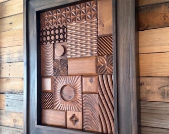 May include: A rectangular wooden wall art piece featuring a dark brown frame and a mosaic of smaller wooden blocks. Each block displays a unique carved texture, including geometric patterns, circular indentations, wavy lines, and smooth surfaces.