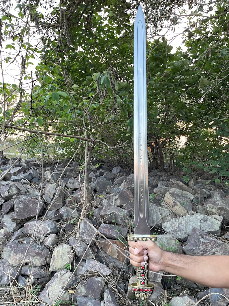May include: A silver sword with a gold hilt and red gems. The sword has a long, straight blade and a pointed tip. The hilt is decorated with intricate designs.