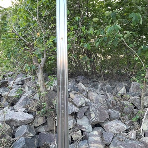 May include: A silver sword with a sharp point and a long, straight blade. The blade has markings on it that read "HFRM-F". The sword is standing upright in a pile of rocks.