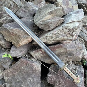 May include: A silver sword with a gold hilt and red gems. The sword is lying on a pile of rocks.