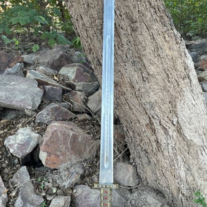 May include: A silver sword with a gold hilt and red gems. The sword is resting on a pile of rocks.