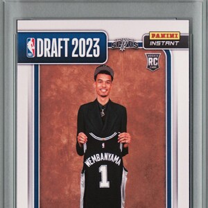 May include: A Rookie Card featuring Victor Wembanyama holding a black and white jersey with the number 1. The card is from the 2023 NBA Draft, with the text "Rookie Card" at the top. The card is encased in a protective holder.