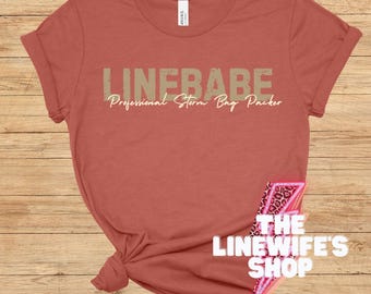 Könnte beinhalten: Ein rostfarbenes T-Shirt mit dem Text "LINEBABE Professional Storm Bag Packer" in hellbraun. Das T-Shirt ist unten verknotet. Der Text "THE LINEWIFE'S SHOP" ist in der unteren rechten Ecke des Bildes sichtbar.