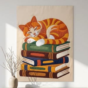 May include: A fabric wall hanging featuring an orange tabby cat with white paws sleeping on a stack of four books. The books are colored green, brown, blue, and yellow, and are stacked on a light beige background. The cat has closed eyes.