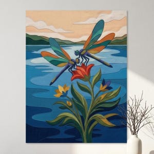 May include: A fabric wall art piece featuring two dragonflies with teal, orange, and purple wings perched on a red flower. The background depicts a blue lake, green hills, and a pale peach sky with clouds, all rendered in layered fabric.