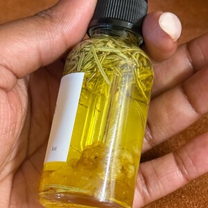 Puede incluir: Una botella de vidrio transparente con un gotero negro en la parte superior llena de un l&iacute;quido amarillo y hierbas verdes. La botella est&aacute; etiquetada con "1oz".