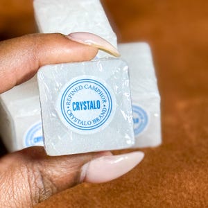 May include: Three white, square-shaped blocks of refined camphor, with a blue and white label that reads "Refined Camphor Crystalo Brand".