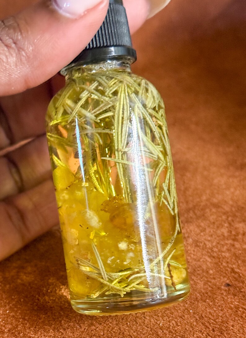 Puede incluir: Una botella de vidrio transparente con un gotero negro en la parte superior llena de un l&iacute;quido amarillo y ramitas de romero verde.