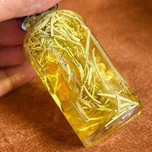 Puede incluir: Una peque&ntilde;a botella de vidrio llena de un l&iacute;quido amarillo y ramitas de romero.