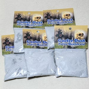 May include: Several bags of Goofer Dust, a product with a Halloween theme. Each bag has a label with a skull, a voodoo doll, and the text "Goofer Dust Polvo Mentecato". The bags are filled with a gray powder.