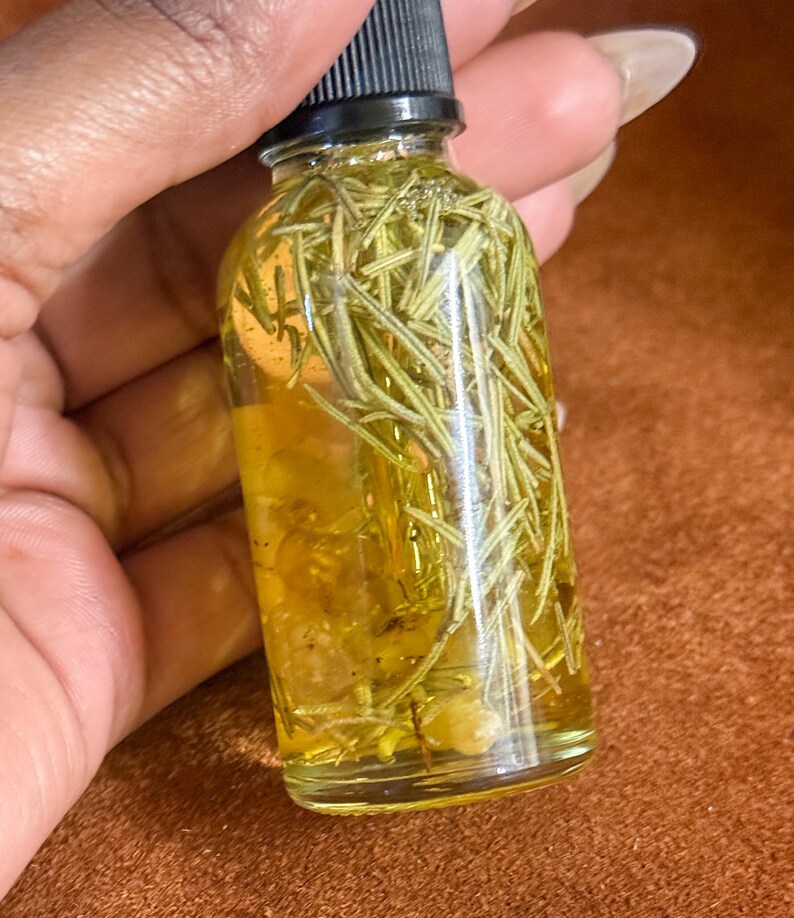 Puede incluir: Una botella de vidrio transparente llena de un l&iacute;quido amarillo y hierbas verdes. La botella tiene una tapa negra y se sostiene en una mano.