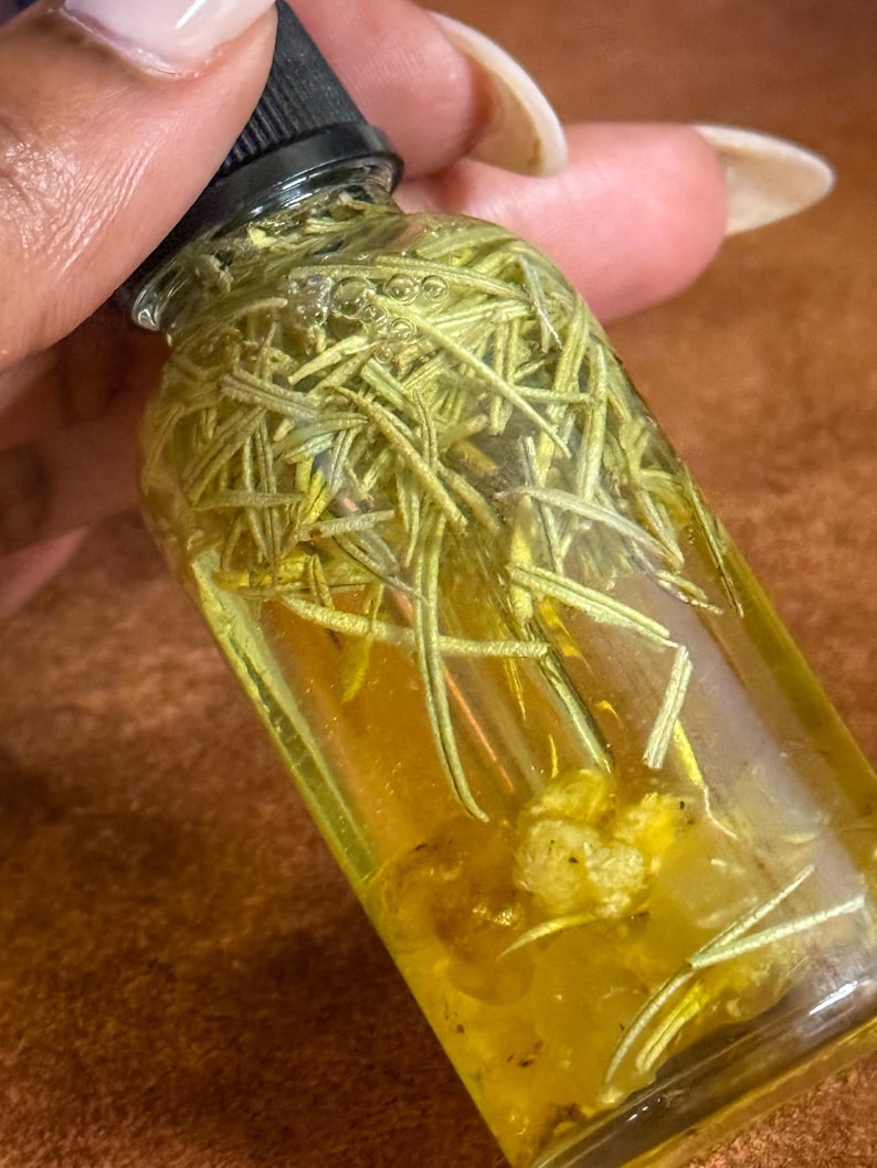 Puede incluir: Una botella de vidrio transparente llena de un l&iacute;quido amarillo y hierbas verdes. La botella tiene una tapa negra.