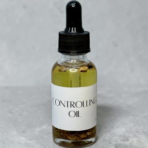 Könnte beinhalten: Eine klare Glastropfflasche gefüllt mit einer hellgelben Flüssigkeit und kleinen pflanzlichen Stücken. Das weiße Etikett trägt den schwarzen Text CONTROLLING OIL. Die Flasche hat einen schwarzen Gummisauger und einen schwarzen Verschluss.