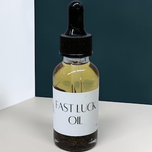 Puede incluir: Un frasco cuentagotas de vidrio transparente lleno de un líquido amarillo dorado con sedimentos botánicos oscuros en la base. El frasco tiene un tapón cuentagotas negro y una etiqueta blanca con el texto "FAST LUCK OIL" impreso en negro.
