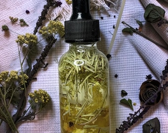 May include: A clear glass dropper bottle with a black cap containing a light yellow liquid infused with green rosemary sprigs and small yellow flower petals. The bottle is cylindrical with a narrow neck and a black rubber bulb dropper top.