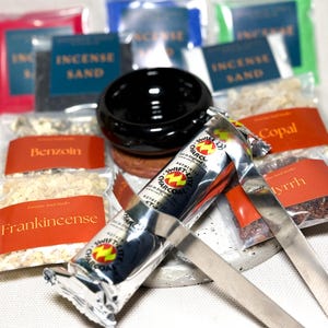 May include: An assortment of incense supplies, including incense sand, charcoal, and various resins like frankincense and myrrh. A black ceramic bowl sits atop a wooden base, with a silver charcoal tube and metal tongs in the foreground. Packaged in colorful bags.
