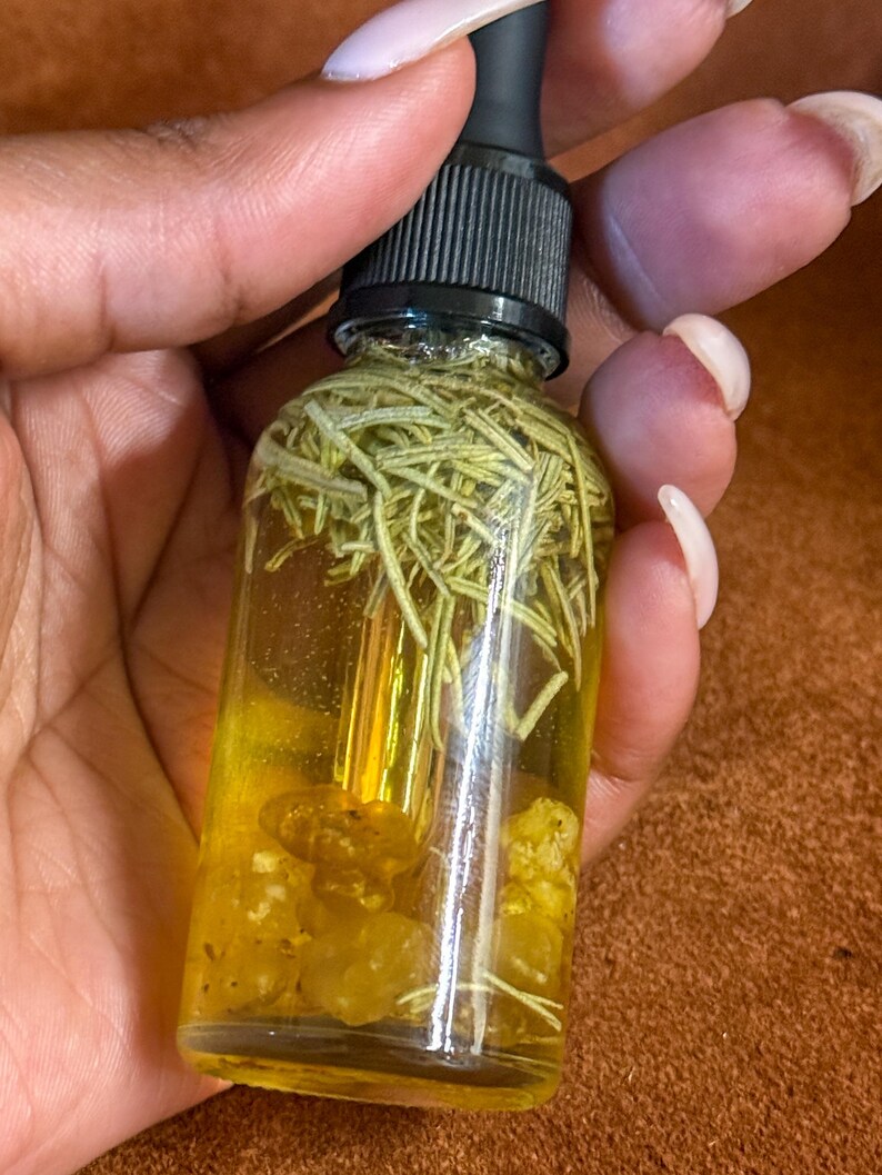 Puede incluir: Una botella de vidrio transparente con un gotero negro en la parte superior llena de un l&iacute;quido amarillo y hierbas verdes. La botella est&aacute; sobre una superficie marr&oacute;n.