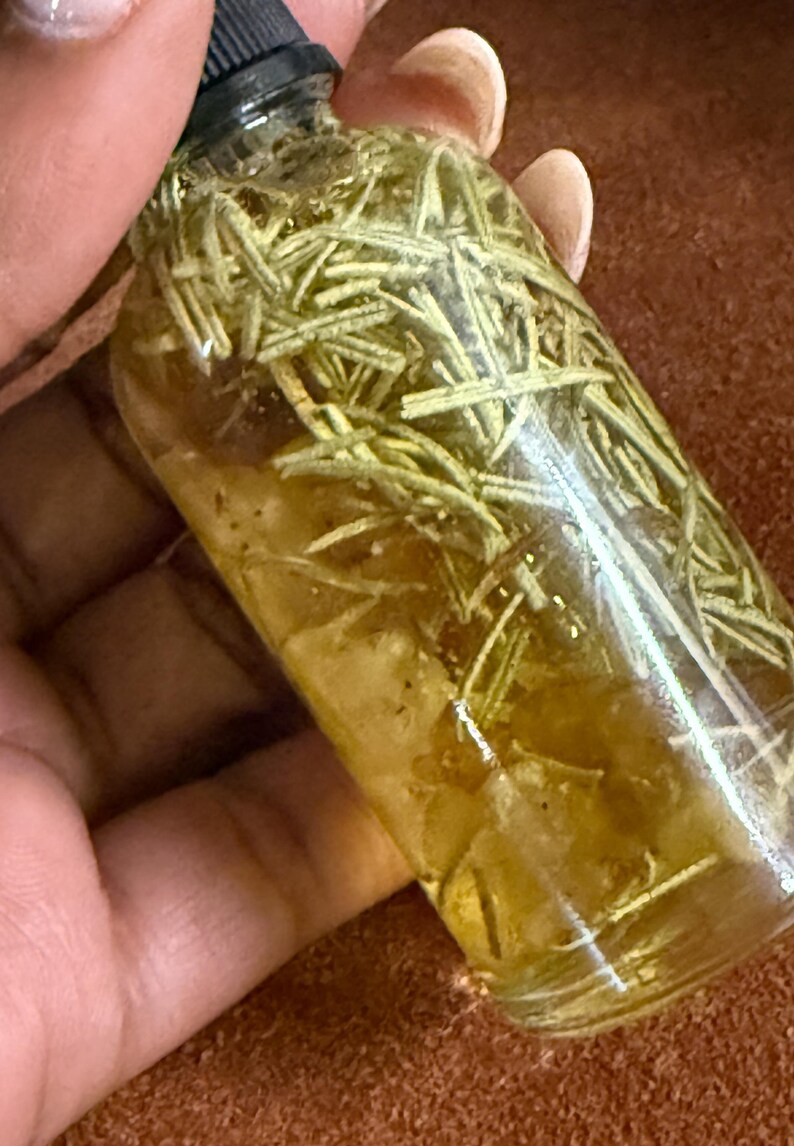 Puede incluir: Una botella de vidrio transparente llena de un l&iacute;quido amarillo y hierbas verdes. La botella tiene una tapa negra.