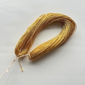 Könnte beinhalten: Eine Spule mit goldenem Metallic-Garn. Das Garn ist gedreht und hat einen dezenten Glanz.