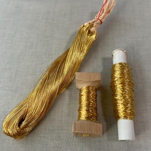 Può includere: Tre bobine di filo metallico dorato, due su bobine di legno e una su una bobina di cartone bianco. Il filo è avvolto attorno alle bobine ed è pronto per essere utilizzato per ricamo o altri lavori manuali.