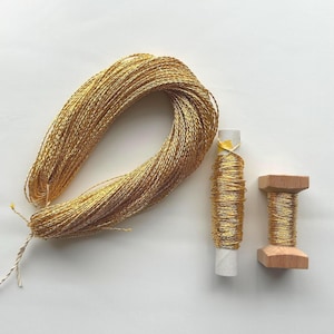 Könnte beinhalten: Eine Spule mit goldenem Metallic-Garn mit zwei kleineren Spulen desselben Garns. Das Garn ist um einen Pappröhre und Holzspulen gewickelt.