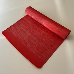 May include: A roll of red fabric with a subtle silver shimmer. The fabric has a textured, striped pattern.