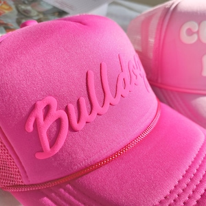 May include: A pink trucker hat with a white mesh back and the word "Bulldog" in raised pink letters.