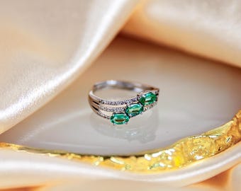 May include: A silver ring with three emerald green oval-shaped gemstones and a row of smaller clear gemstones.
