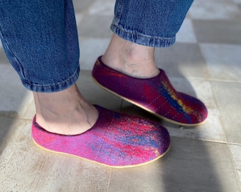 May include: A pair of colorful wool slippers with a red, blue, and yellow pattern. The slippers are worn on a tiled floor.