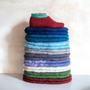 Op de afbeelding: Een stapel kleurrijke viltcirkel in tinten blauw, groen, grijs, paars en rood. De bovenste cirkel heeft een rode viltpantoffel erop.