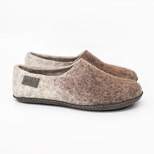 Könnte beinhalten: Ein Paar braune und beige Filzschuhe mit einer dunkelgrauen Sohle. Die Schuhe haben ein strukturiertes Aussehen und ein kleines Etikett mit der Aufschrift "BURE BROS". Die Schuhe sind für den Innenbereich konzipiert.