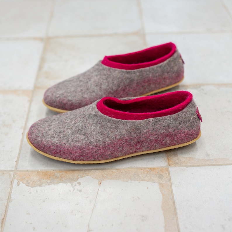 K&ouml;nnte beinhalten: Ein Paar graue Filzpantoffeln mit rosa Besatz. Die Pantoffeln haben eine abgerundete Spitze und eine flache Sohle.