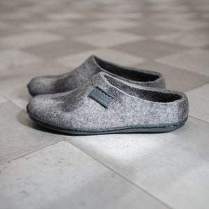 May include: A pair of gray felt slippers with a black leather trim and a small gray label on the top of the slipper.
