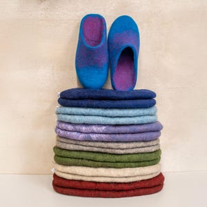 Könnte beinhalten: Ein Stapel bunter Filzpantoffeln in verschiedenen Blautönen, Lila, Grün, Beige und Rot. Die Pantoffeln sind in einem Stapel angeordnet, wobei die beiden oberen Pantoffeln ein Paar blaue und lila Pantoffeln sind.