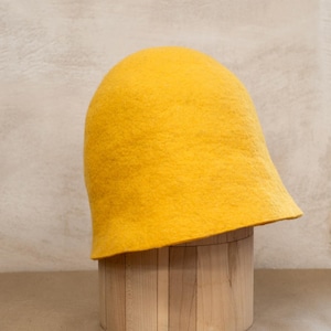 May include: A bright yellow felted wool hat with a rounded crown and a slightly flared brim. The hat features a dense, textured surface characteristic of felted material, showcasing a solid, vibrant colour throughout its entire structure.