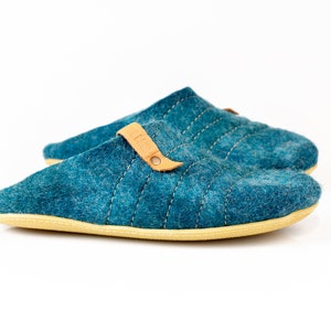 May include: A pair of teal blue felt slippers with a brown leather strap and a beige sole.