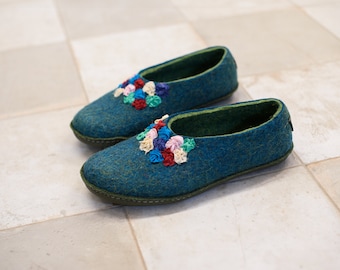 Può includere: Un paio di pantofole in feltro blu con bordi verdi e fiori di stoffa colorati.